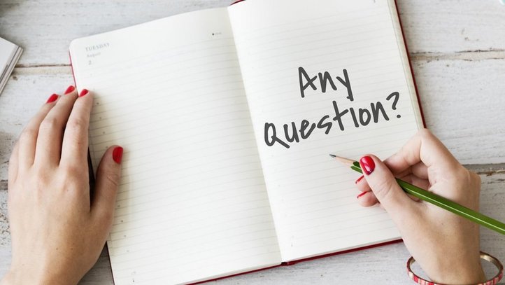 eine Frau schreibt in ein Heft "any questions?"