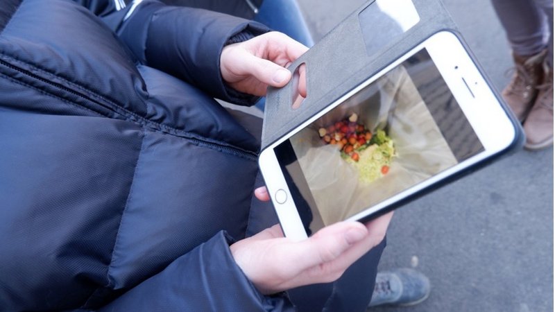 Person fotografiert den Lebensmittel Einkauf in einer Plastiktüte mit dem Smartphone