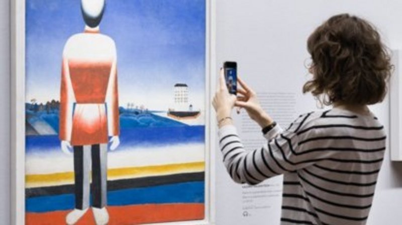 Frau steht mit einem Handy vor einem Gemälde