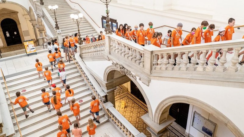 Kinder in orangenen Shirts in prunkvollem Stiegenhaus
