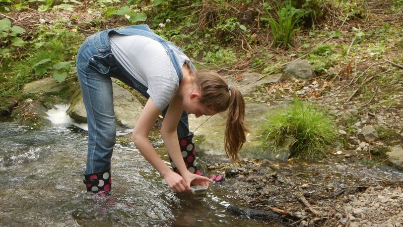 eine Schülerin entnimmt in der Natur eine Wasserprobe