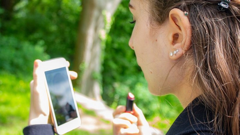 Eine Frau schminkt sich die Lippen und benutzt ihr Smartphone als Spiegel