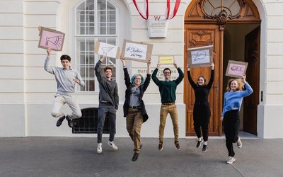 Junge Studierende hüpfen in die Luft und halten Schilder in der Hand