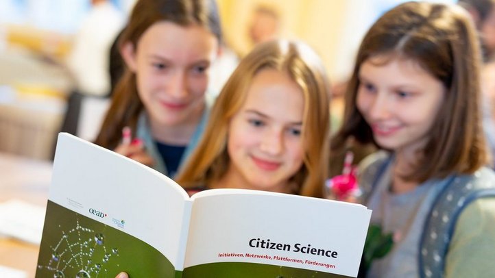 Drei Schülerinnen werfen einen Blick in die Citizen-Science-Broschüre