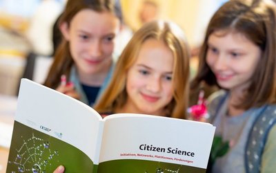 Drei Schülerinnen werfen einen Blick in die Citizen-Science-Broschüre